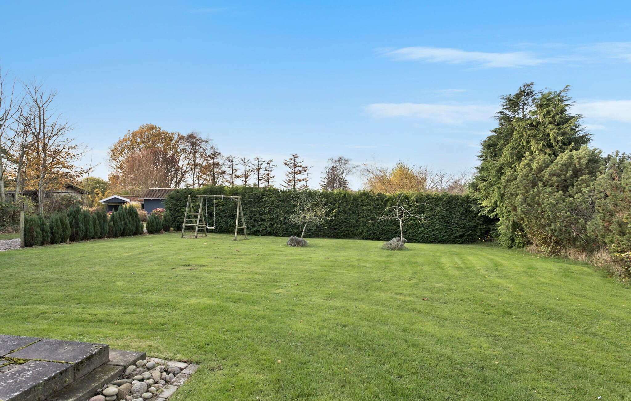 A well-maintained backyard with a wooden swing set, a stone wall, and a hedge.