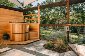 Un sauna en bois avec une porte en métal, entouré d’une terrasse en bois et doté d’un sol en pierre.