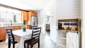 A kitchen with wooden cabinets, a refrigerator, a dining table with chairs, and a coffee station.