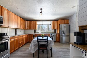A kitchen with wooden cabinets, a dining table with chairs, a refrigerator, and a coffee maker. - Every Season Get Away (Alexandria)