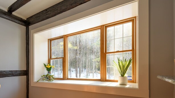 A room with a large window, wooden beams, and a potted plant on the windowsill.