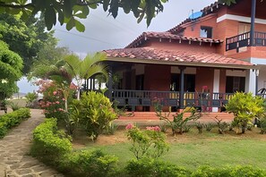 A two-story building with a red-tiled roof, a covered porch, and a garden with various plants and flowers. - Hotel San  Miguel Barichara  Campestre (Barichara)