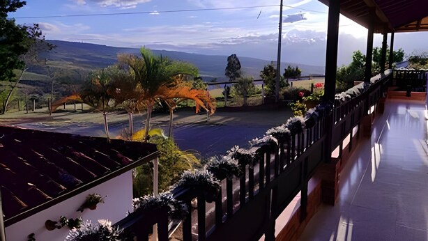 A balcony with a view of a valley, a road, and a helicopter in the distance.