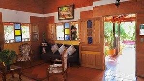 A cozy room with a wooden ceiling, a sofa, a chair, and a wooden door leading outside.