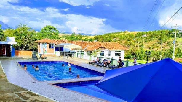 A swimming pool with lounge chairs and a blue umbrella, surrounded by buildings and greenery. - Hotel San  Miguel Barichara  Campestre (Barichara)
