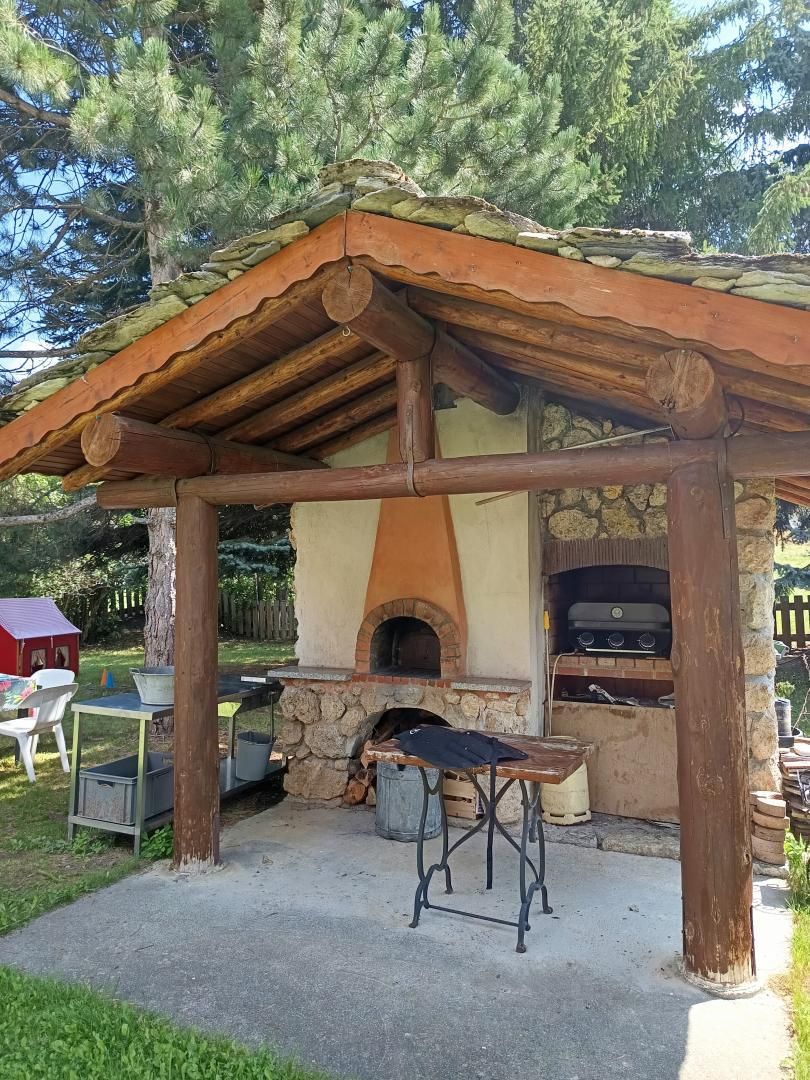 Un área rústica para cocinar al aire libre con un horno de piedra, mesas de madera y un espacio de estar cubierto.