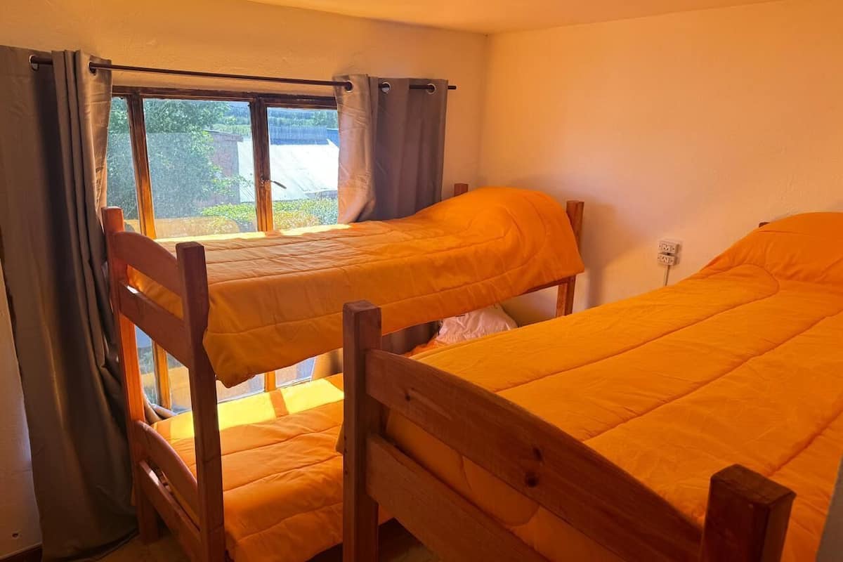 A room with two bunk beds, a window with curtains, and a visible outdoor view.