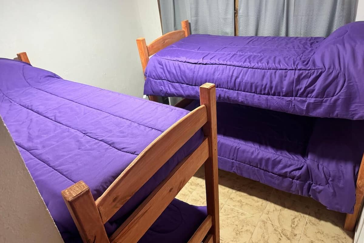 A room with two wooden bunk beds with purple bedding.