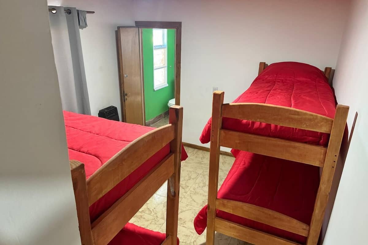 A room with two wooden bunk beds with red bedding, a green door, and a white wall.
