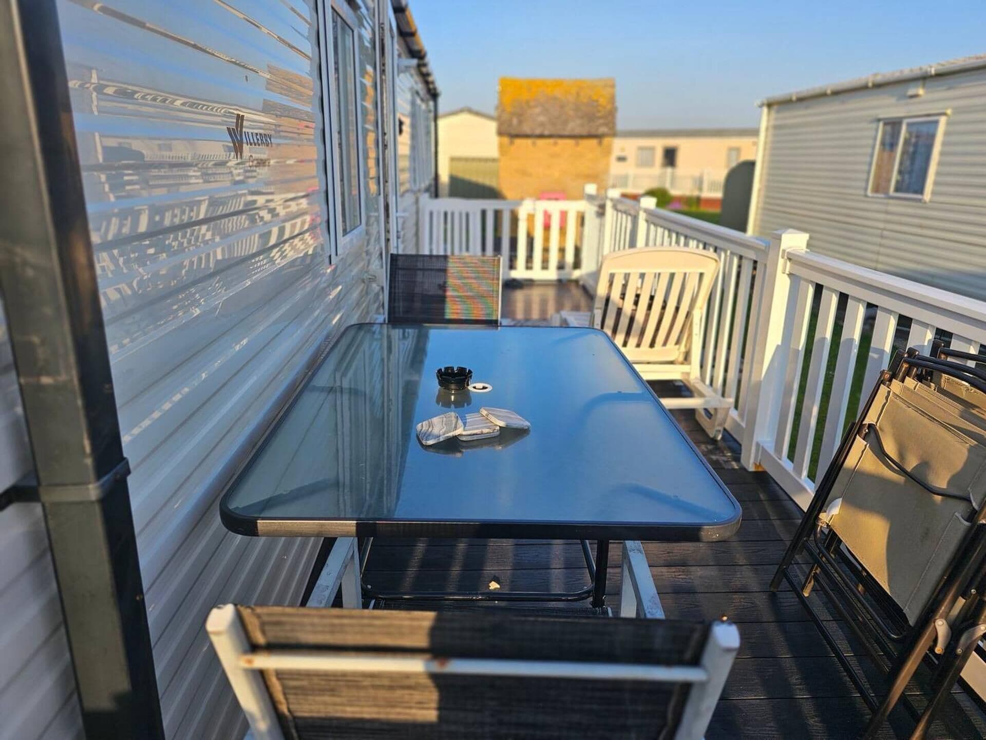Terraza con mesa y sillas, una mesita con un libro y una taza, y barandilla blanca.