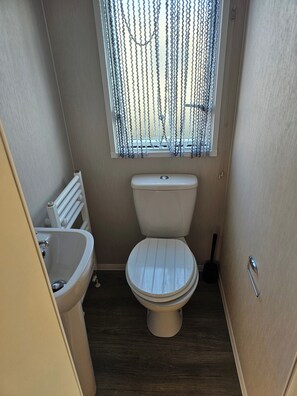 Een kleine badkamer met toilet, wastafel en raam met gordijntje.