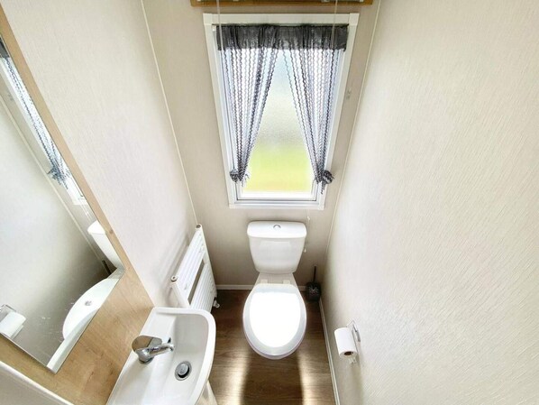 Un baño pequeño con inodoro, lavamanos y ventana con cortinas.