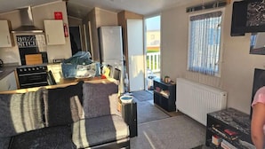 Un ambiente compatto con angolo cottura, divano, termosifone e finestra con tende.