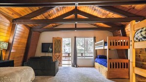 Acogedor dormitorio en ático con paredes de madera y techo inclinado, que incluye una cama individual superior y otra inferior, un sofá y un televisor.