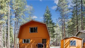 Una cabaña de dos pisos con balcón, rodeada por un bosque.