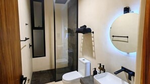 A modern bathroom with a toilet, a sink, a mirror, and a shower area. - Koom (Tulum)