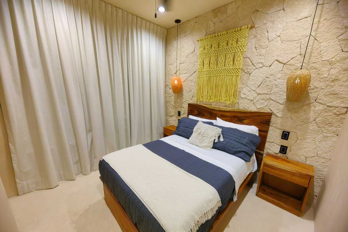 A bedroom with a bed, curtains, a wall-mounted lamp, and a textured wall.