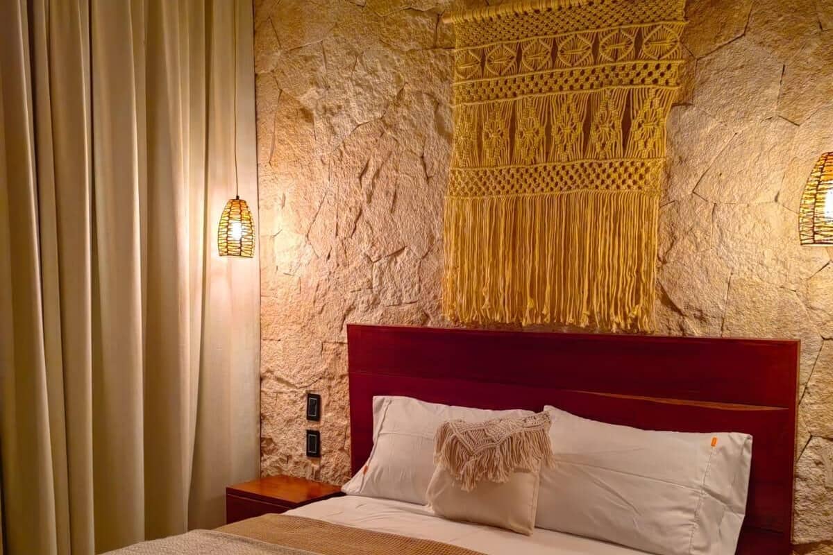 A bedroom with a stone wall, a red headboard, a bed with white linens, and a wall-mounted air conditioner.