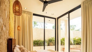 A bedroom with a bed, a ceiling fan, a bedside table, and a view of the outdoors. - Koom (Tulum)