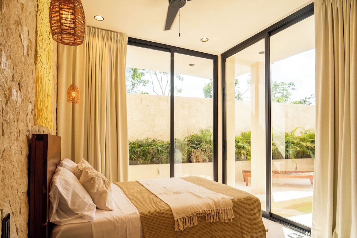 A bedroom with a bed, a ceiling fan, a bedside table, and a view of the outdoors.