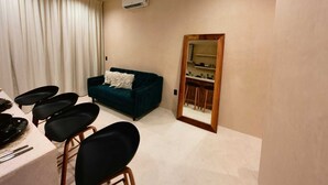 A compact living space with a dark blue sofa, a dining table with black chairs, and a mirrored wardrobe. - Koom (Tulum)