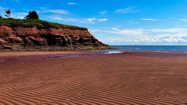 A beach with red sand and a rocky cliff.