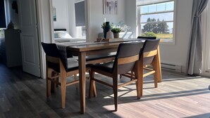 A dining area with a wooden table and chairs, a view of a bedroom through an open door, and a window with blinds.