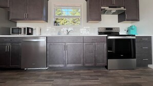 A modern kitchen with dark cabinets, stainless steel appliances, and a window above the sink.