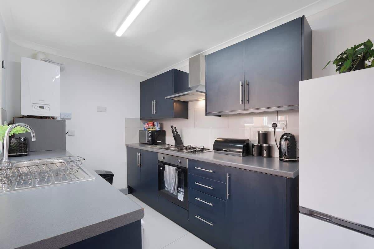 A modern kitchen with dark cabinets, a built-in oven, a coffee maker, and a kettle.