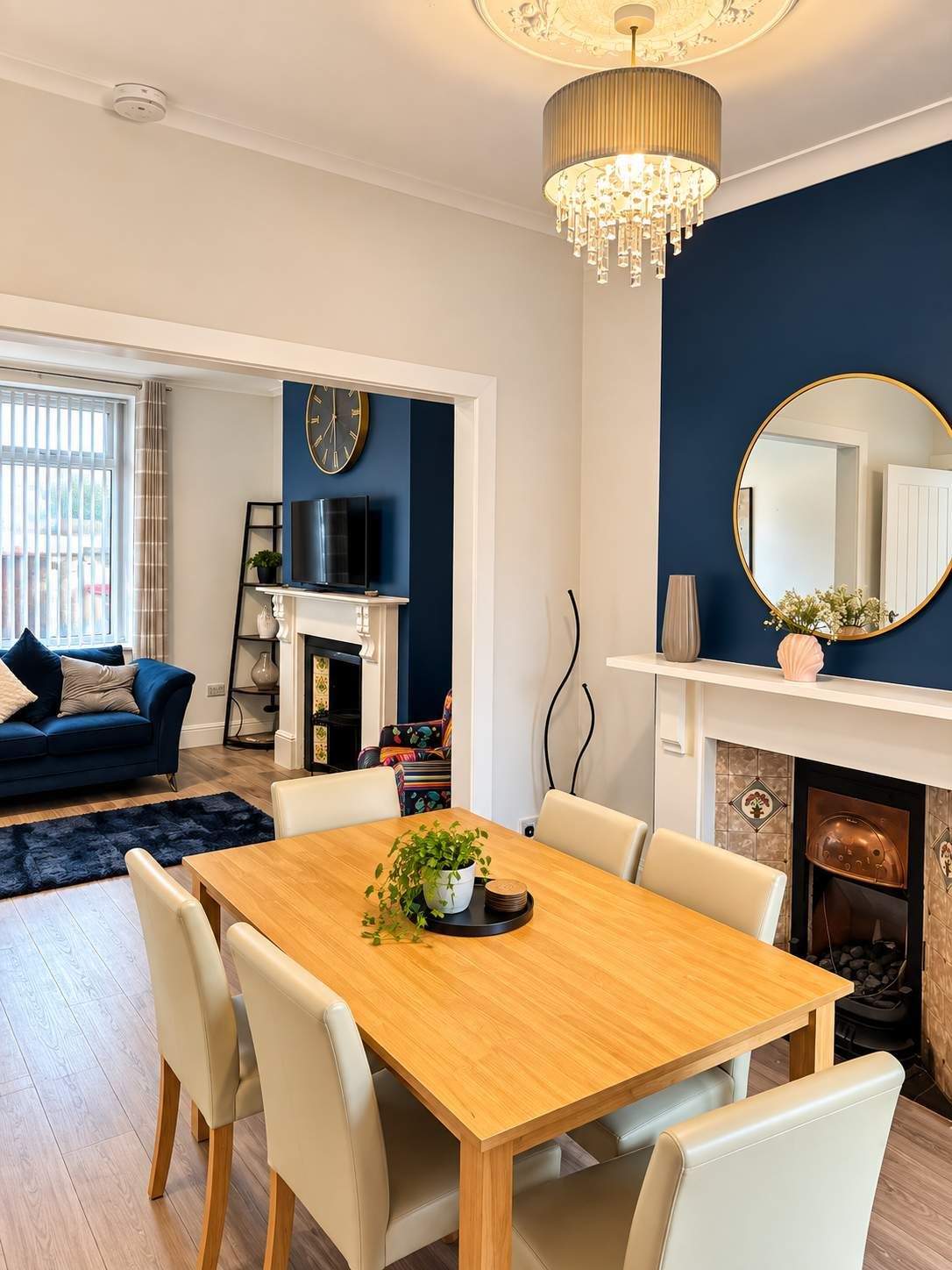 A dining area with a wooden table, white chairs, a chandelier, and a blue accent wall.
