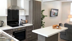 Une cuisine moderne dotée d’un îlot central, d’un four encastré et d’un coin repas avec un canapé gris.