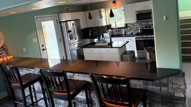 A kitchen with a central island, white cabinets, a stainless steel refrigerator, and a stone backsplash. - Wine Country Oasis Pool/Sleeps 14 (Kerrville)