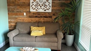 A room with a wooden wall panel, a sofa with yellow cushions, a white coffee table with a basket, and a large potted plant. - Wine Country Oasis Pool/Sleeps 14 (Kerrville)