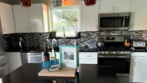 A modern kitchen with white cabinets, a black countertop, a stainless steel stove, a microwave, and a window with a view of greenery outside. - Wine Country Oasis Pool/Sleeps 14 (Kerrville)