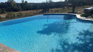 A clear, blue swimming pool with a stone border, surrounded by a grassy area and trees. - Wine Country Oasis Pool/Sleeps 14 (Kerrville)