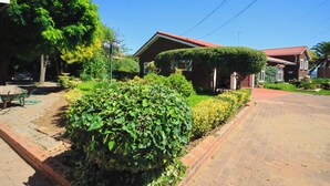 A residential area with a paved driveway, a wheelbarrow, and well-maintained hedges. - The Advocate Suites Manor (Maseru)