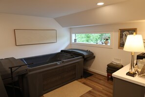Un cuarto de spa con un jacuzzi, una ventana con vistas a follaje, un cuadro en la pared y una lámpara sobre la mesita de noche.