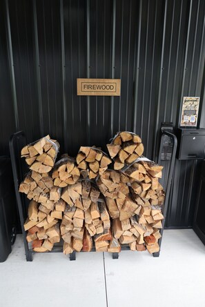 A stack of firewood labeled 'FIREWOOD' in front of a black metal wall.