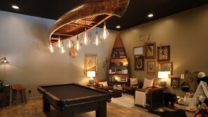 A pool table in a room with a wooden floor, a bookshelf, and a lamp. - Creative Cabins - Hayloft (Logan)