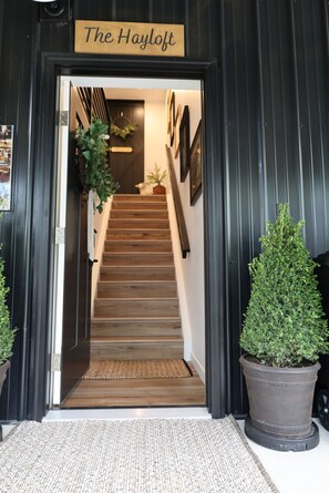 Un escalier en bois mène à une pièce sur laquelle est apposée une pancarte indiquant : « Le grenier à foin ».