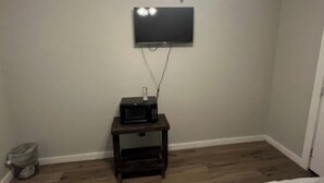 A bedroom with two beds, a ceiling fan, a TV mounted on the wall, and a small table with a microwave.