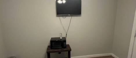 A bedroom with two beds, a ceiling fan, a TV mounted on the wall, and a small table with a microwave.
