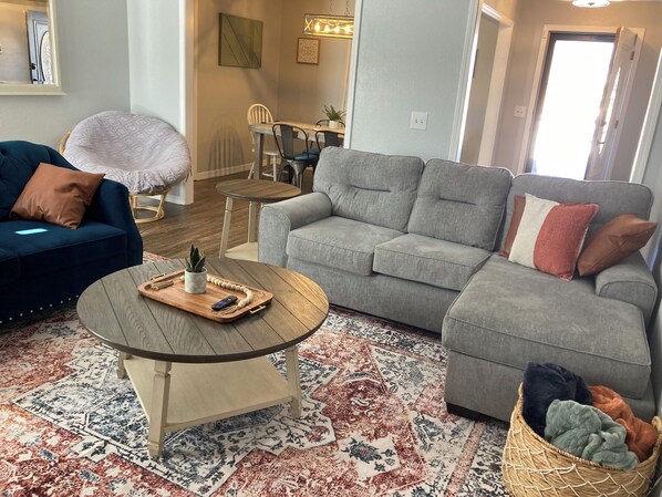 Ein Wohnzimmer mit einem blauen Sofa, einem grauen Sofa, einem Holztisch und einem gemusterten Teppich.