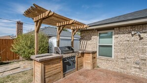 Cocina exterior con parrilla, horno y pérgola de madera.