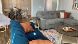 Una sala de estar con un sofá azul, un sofá seccional gris y una mesita redonda con una planta.