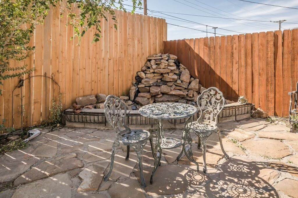 A patio with stone flooring, metal chairs, a round table, and a stone fireplace.