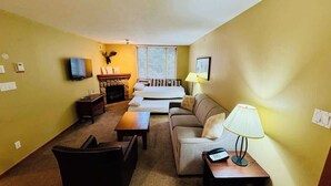 Ett kompakt hotellrum med en soffa, ett litet bord, en lampa, en TV och en öppen spis.