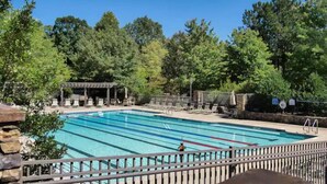 Piscina rectangular con múltiples carriles, rodeada de sillas de descanso y una zona de estar cubierta.