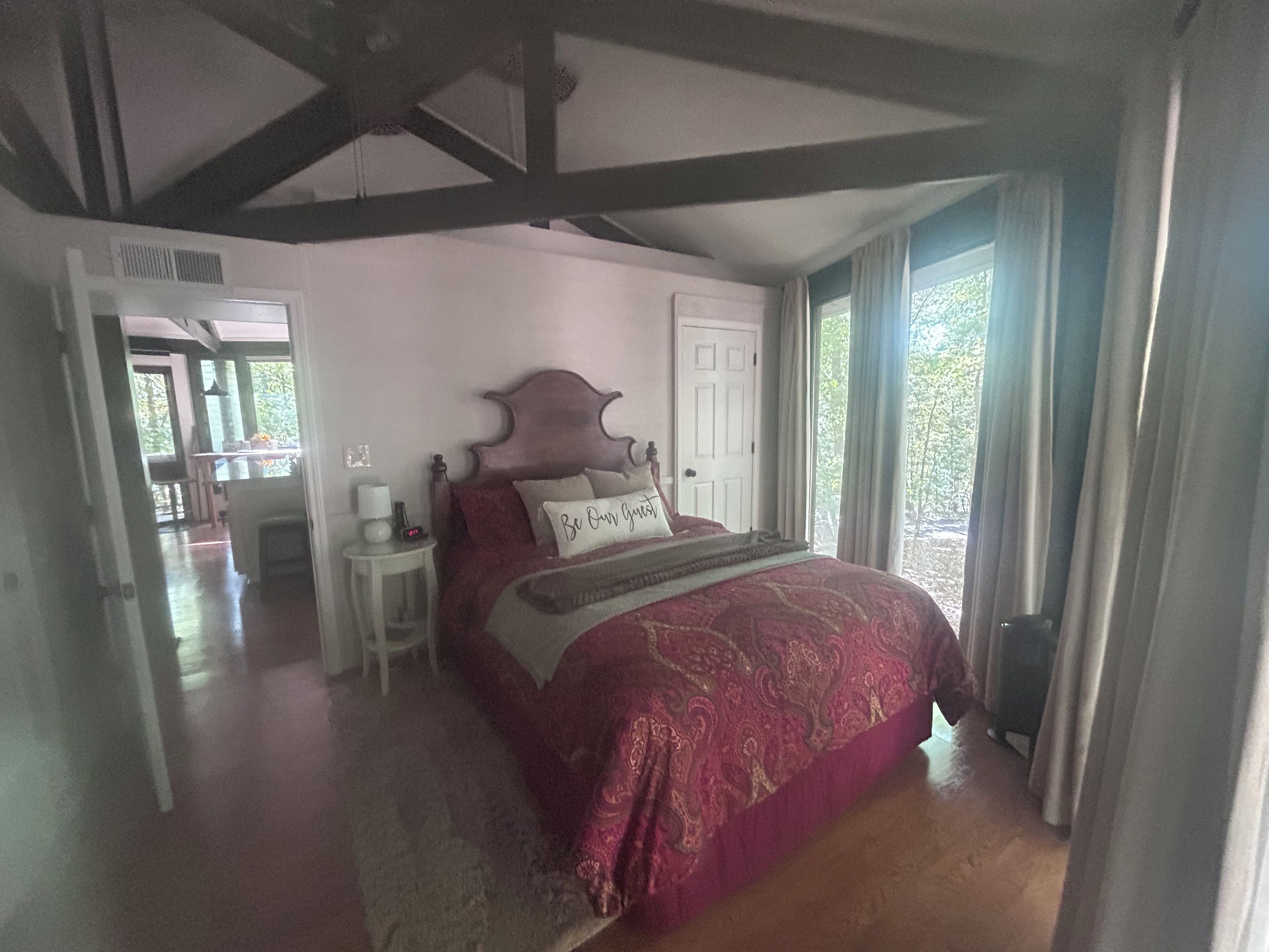 A bedroom with a large bed, a nightstand, a door leading to another room, and a window with curtains.