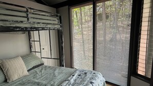 Un dormitorio con cama, ventana con persianas y vistas a árboles.